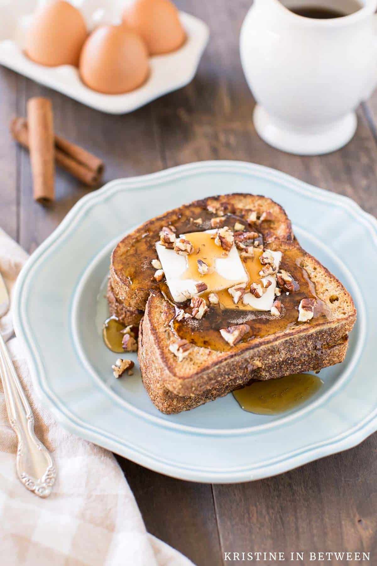 Two slices of pumpkin French toast sitting on a blue plate with butter, syrup, and pecans on top.