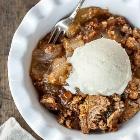 A bowl of caramel apple dump cake with a scoop of vanilla ice cream on top.