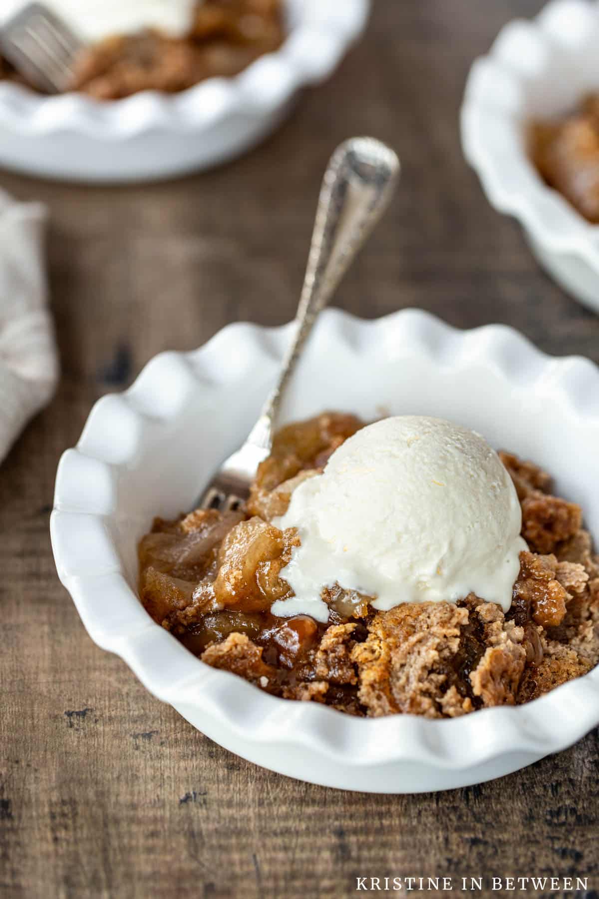 A bowl of caramel apple dump cake with a scoop of vanilla ice cream on top.