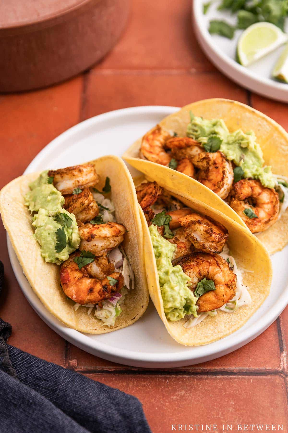 Three air fryer shrimp tacos with avocado on top sitting on a white plate.