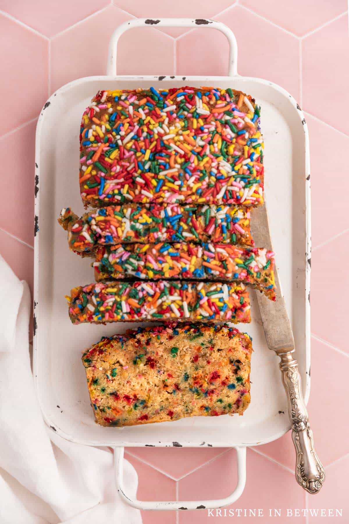 Slices of sugar cookie banana bread laying on a white tray with a white napkin and an antique knife.