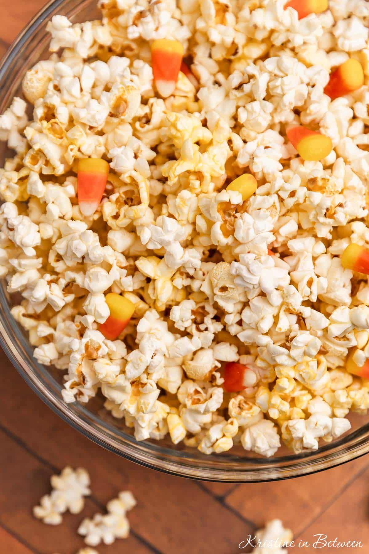 Popcorn and candy corn in glass bowls with some popcorn scattered around.