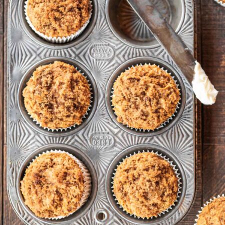 Pumpkin muffins with a crumb topping in a muffin tin with a knife sitting next to them.
