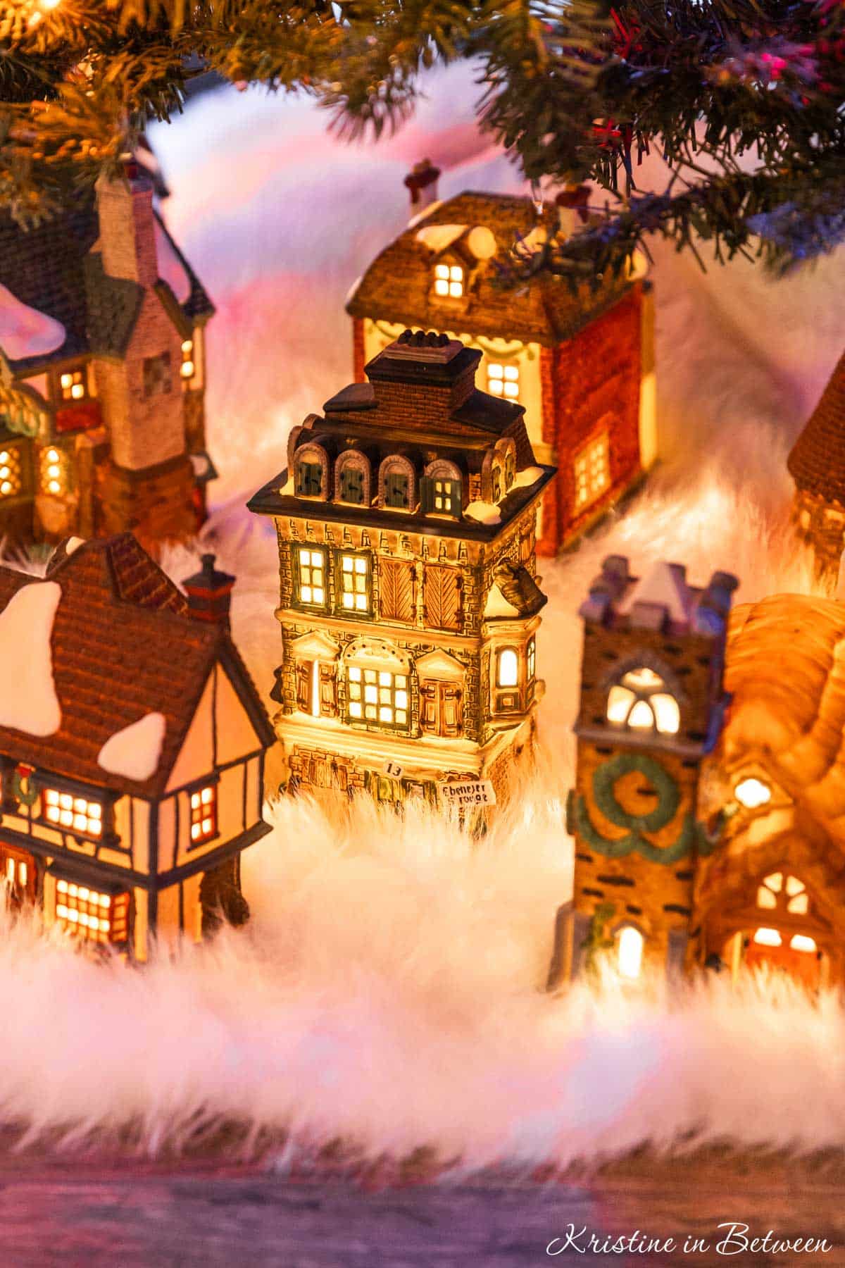 A glowing vintage Christmas village on a white tree skirt under a Christmas tree.
