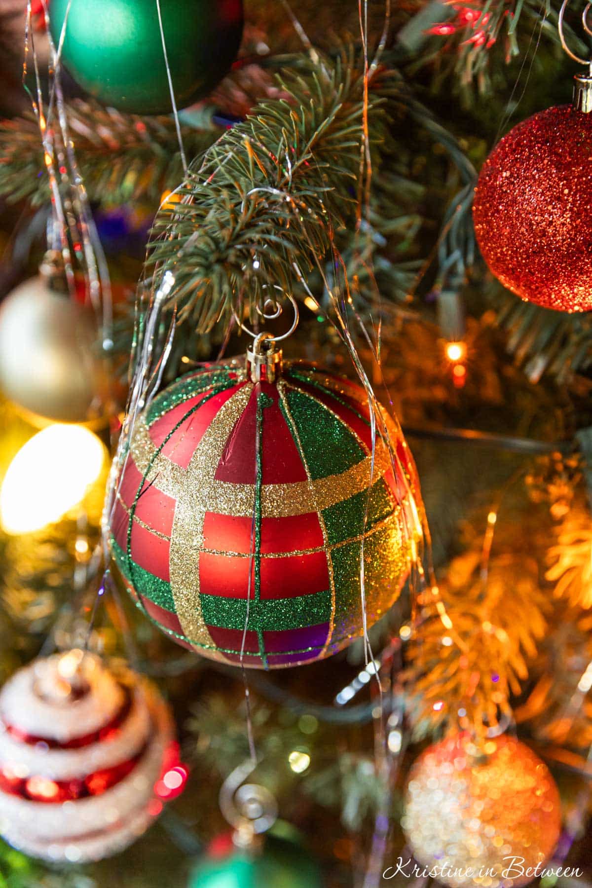 A red ornament on a Christmas tree with tinsel on top.