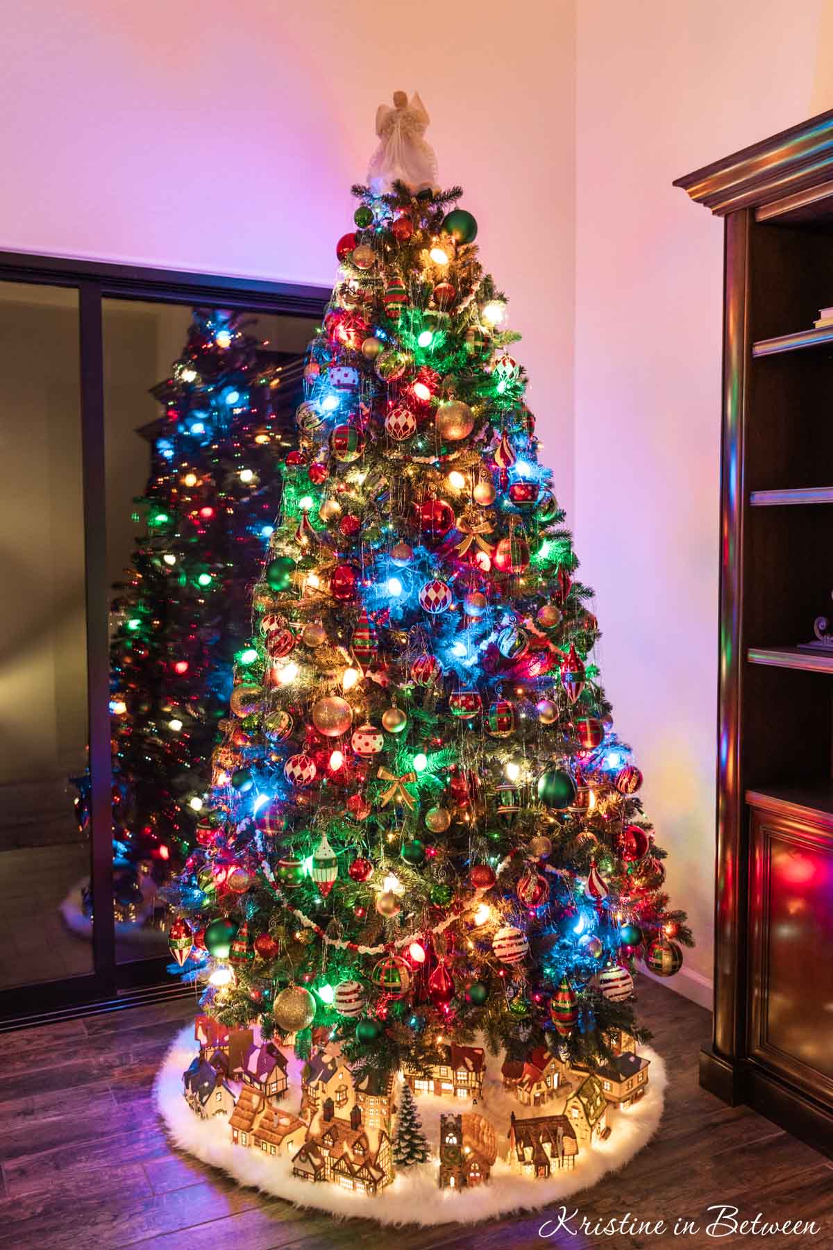 A traditional Christmas tree with a Christmas village underneath it.