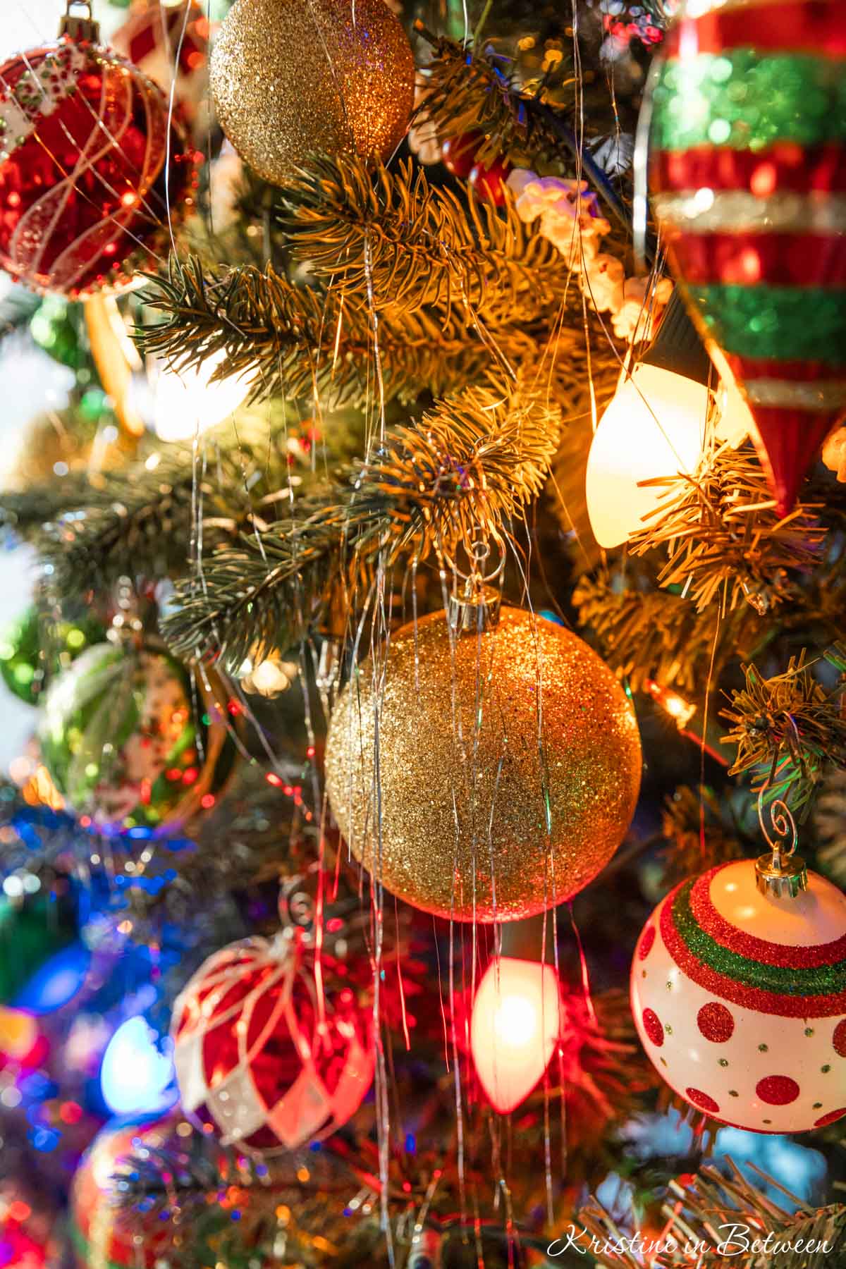 Tinsel and traditional colored ornaments hanging on a Christmas tree.