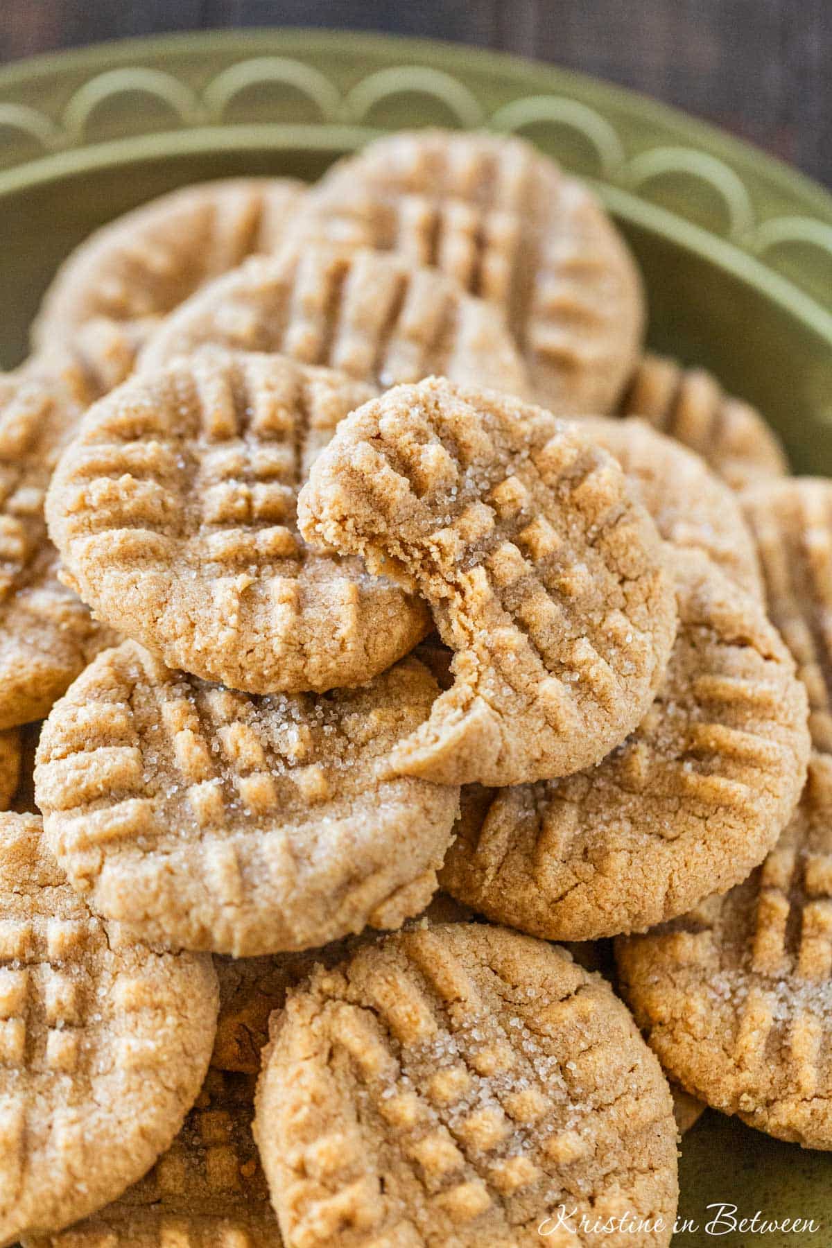 3 ingredient peanut butter cookies laying on a green plate with a small cup of peanut butter next to them.
