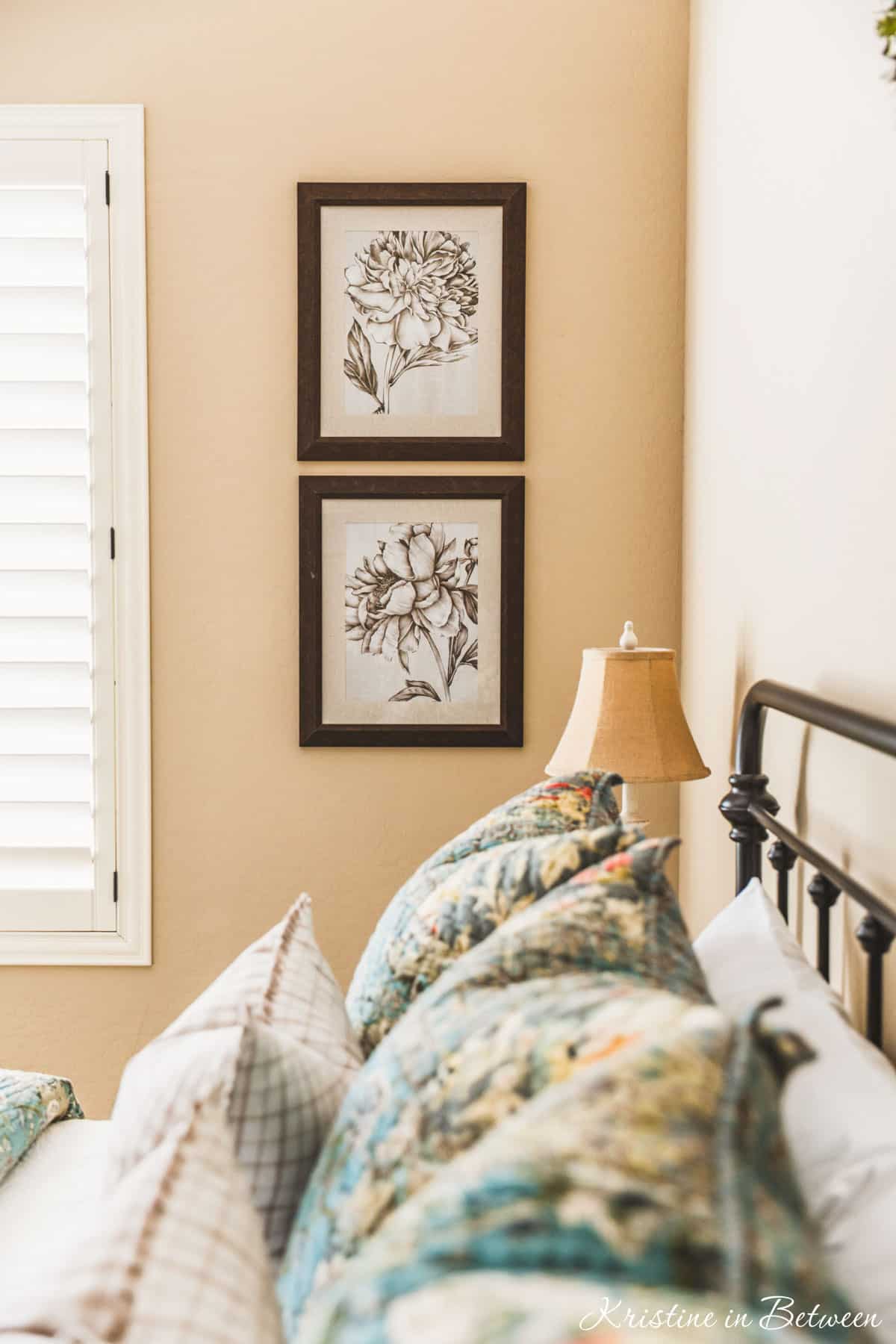 A guest bedroom with blue quilted bedding, a metal bed, and some floral artwork on the wall.