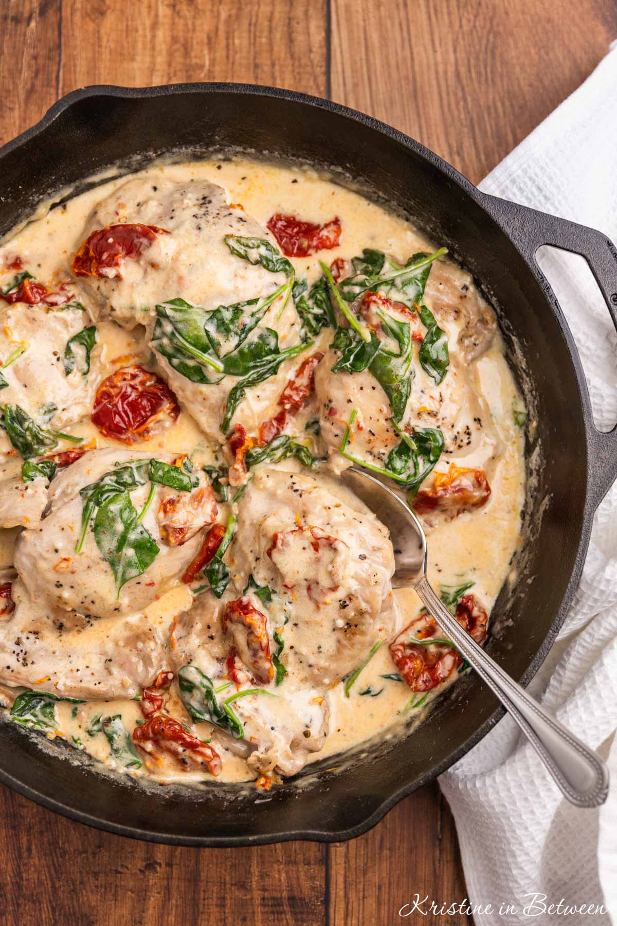 Creamy Tuscan chicken thighs in a cast iron pan with a spoon.