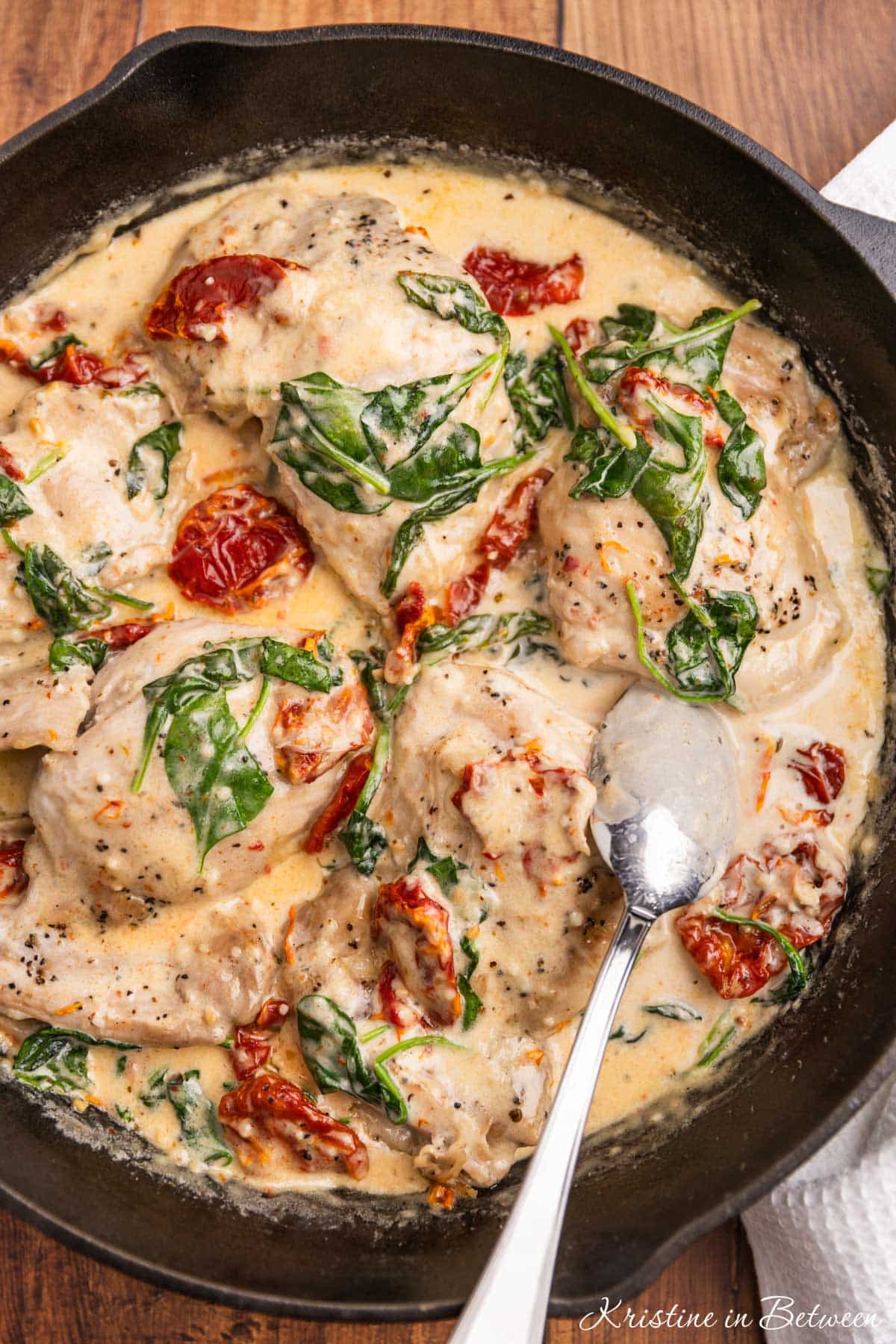 Tuscan chicken thighs with spinach and sun dried tomatoes in a cast iron pan.