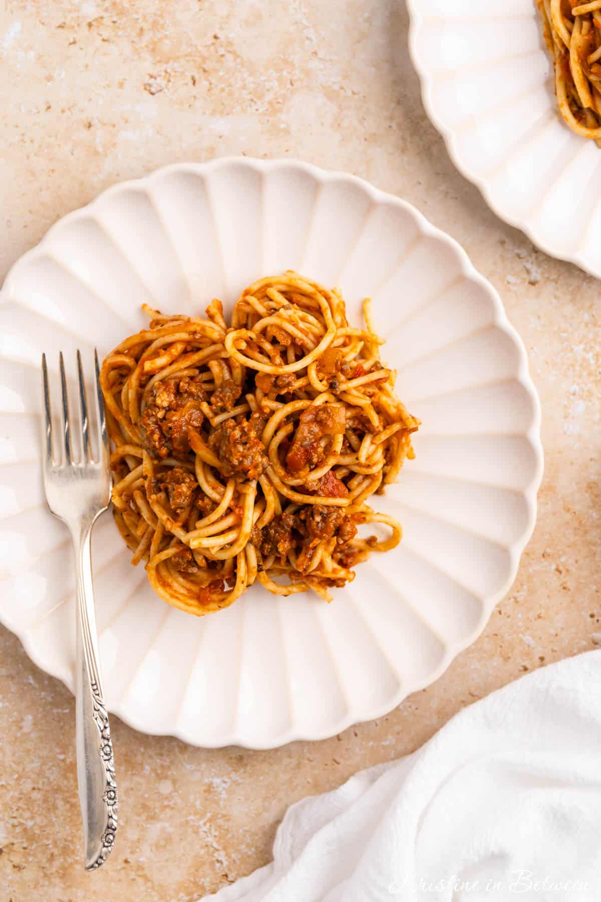A plate of spaghetti with meat sauce with a fork sitting next to it.