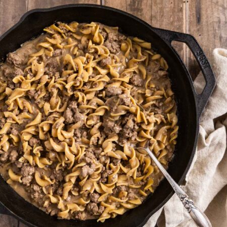 A skillet of beef stroganoff with egg noodles with a spoon in it.