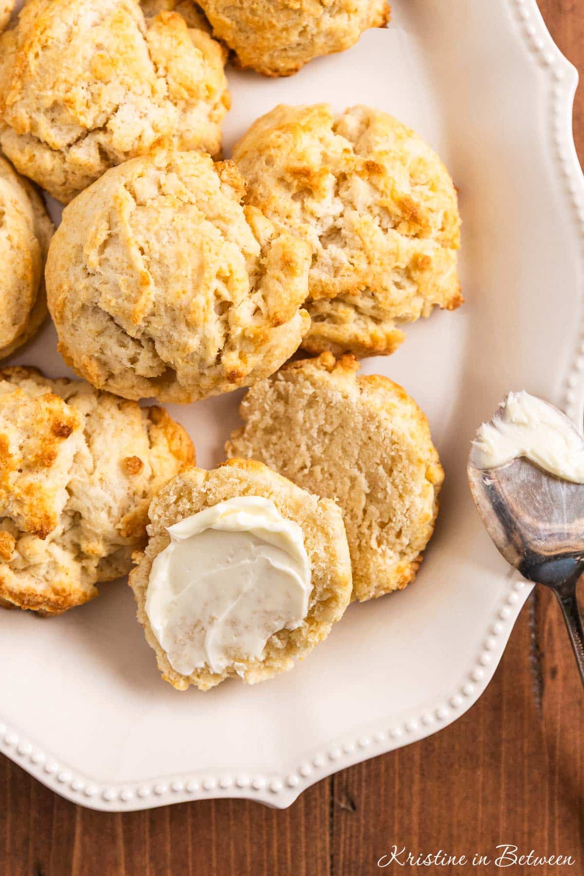 Homemade biscuits on a plate with one cut in half and lightly buttered.