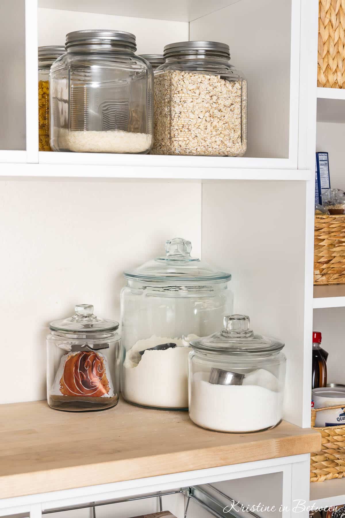 Several different glass jars and canisters with pantry ingredients in them.
