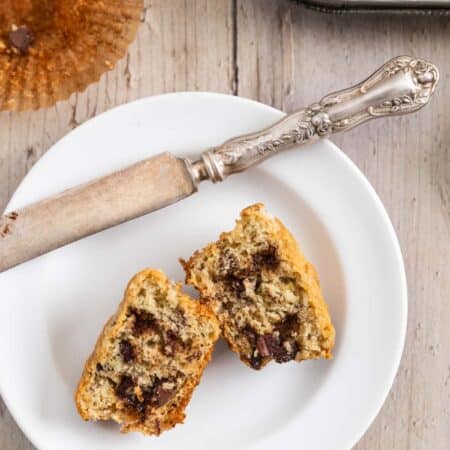 A muffin on a white plate that's cut in half with a knife next to it.