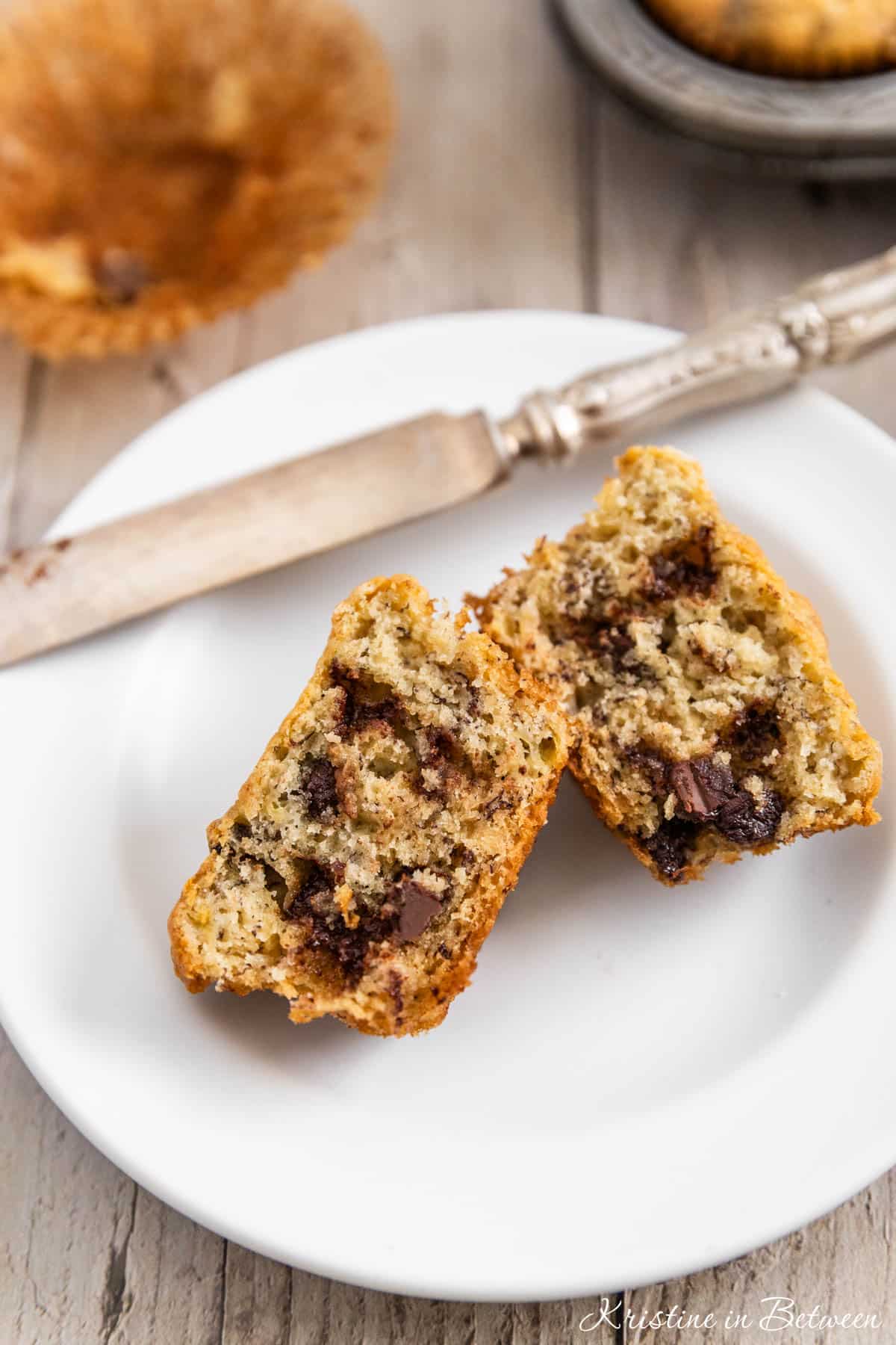A muffin on a white plate that's cut in half with a knife next to it.