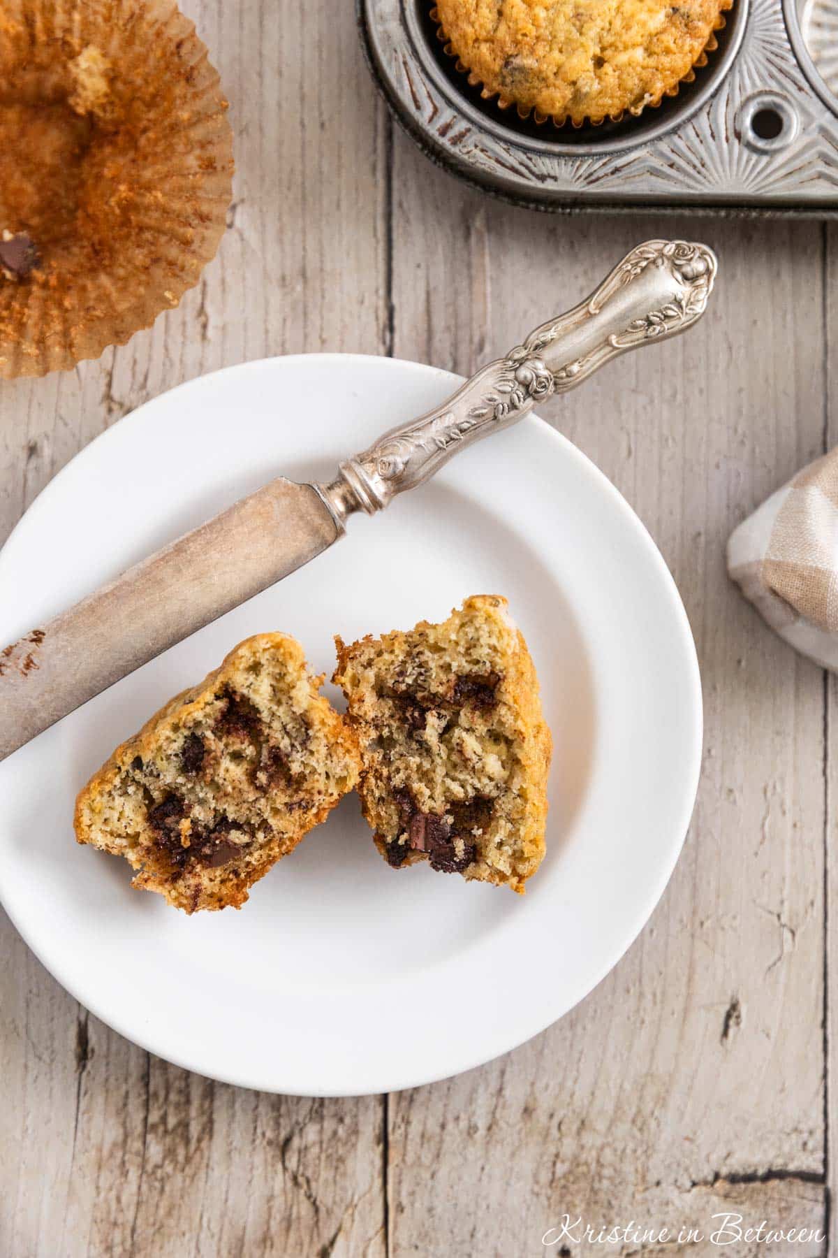A muffin on a white plate that's cut in half with a knife next to it.