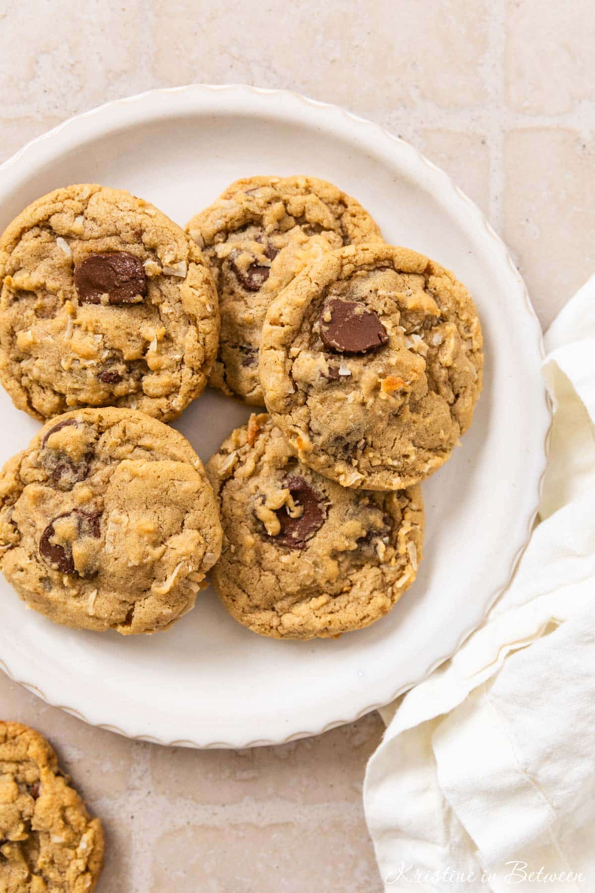 A plate of chocolate chip coconut cookies with a white napkin laying next to them.