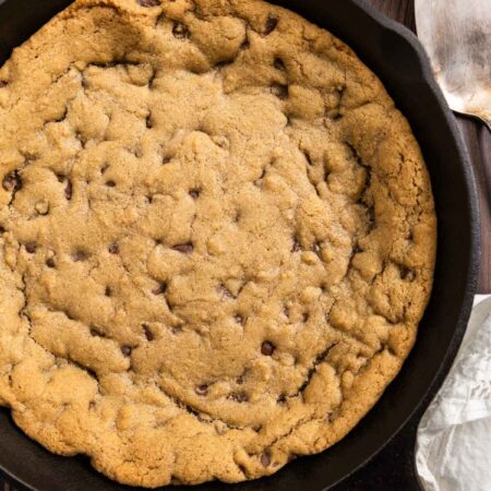 A skillet chocolate chip cookie in a cast iron pan with a spatula next to it.