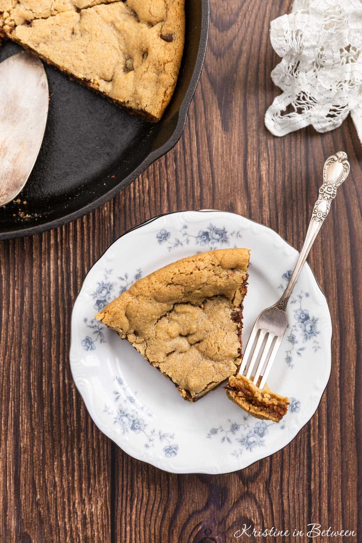 A bite of a skillet cookie on a fork with the rest of the slice on a plate.