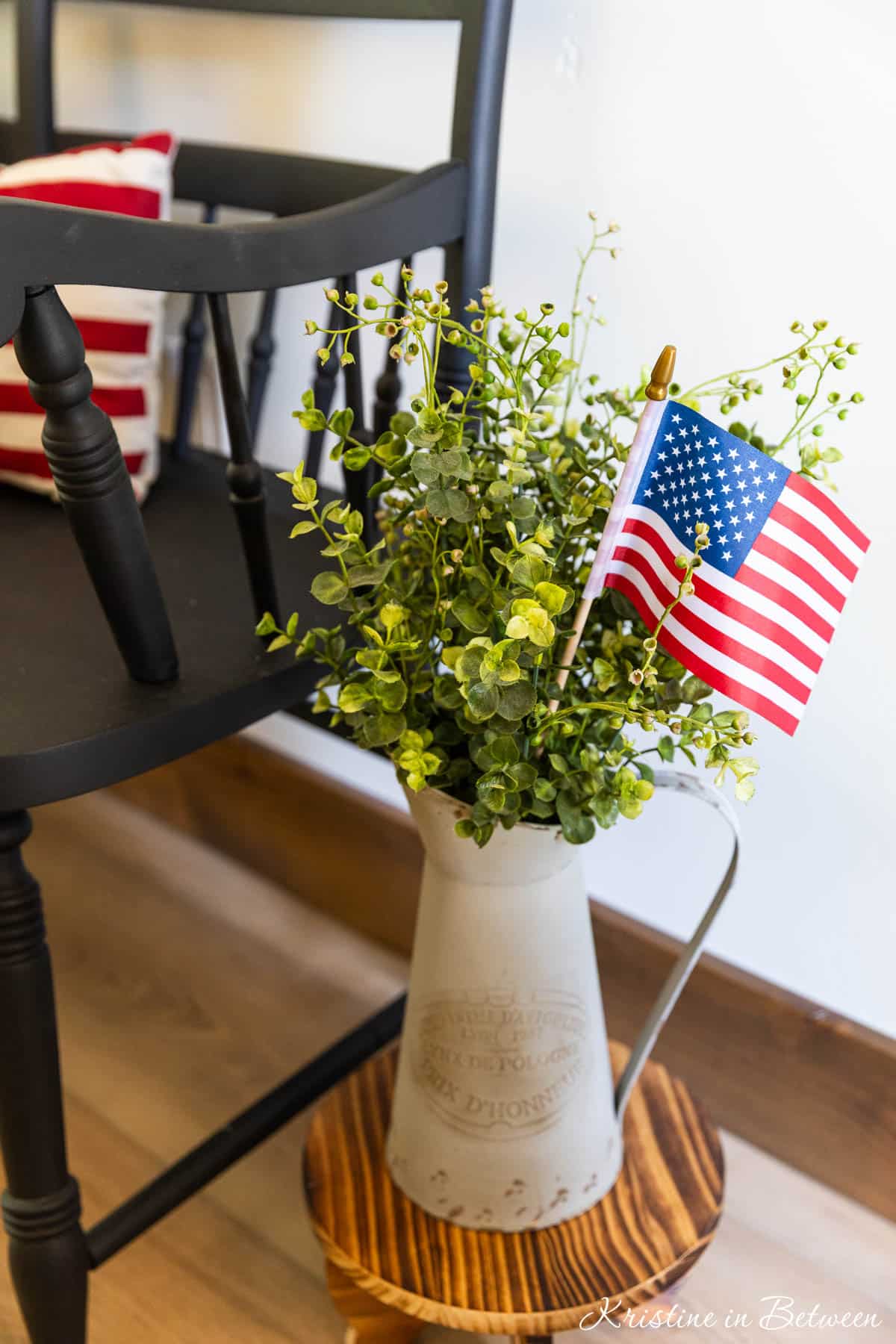 A pitcher of greenery with a flag in it, sitting next to a black bench.